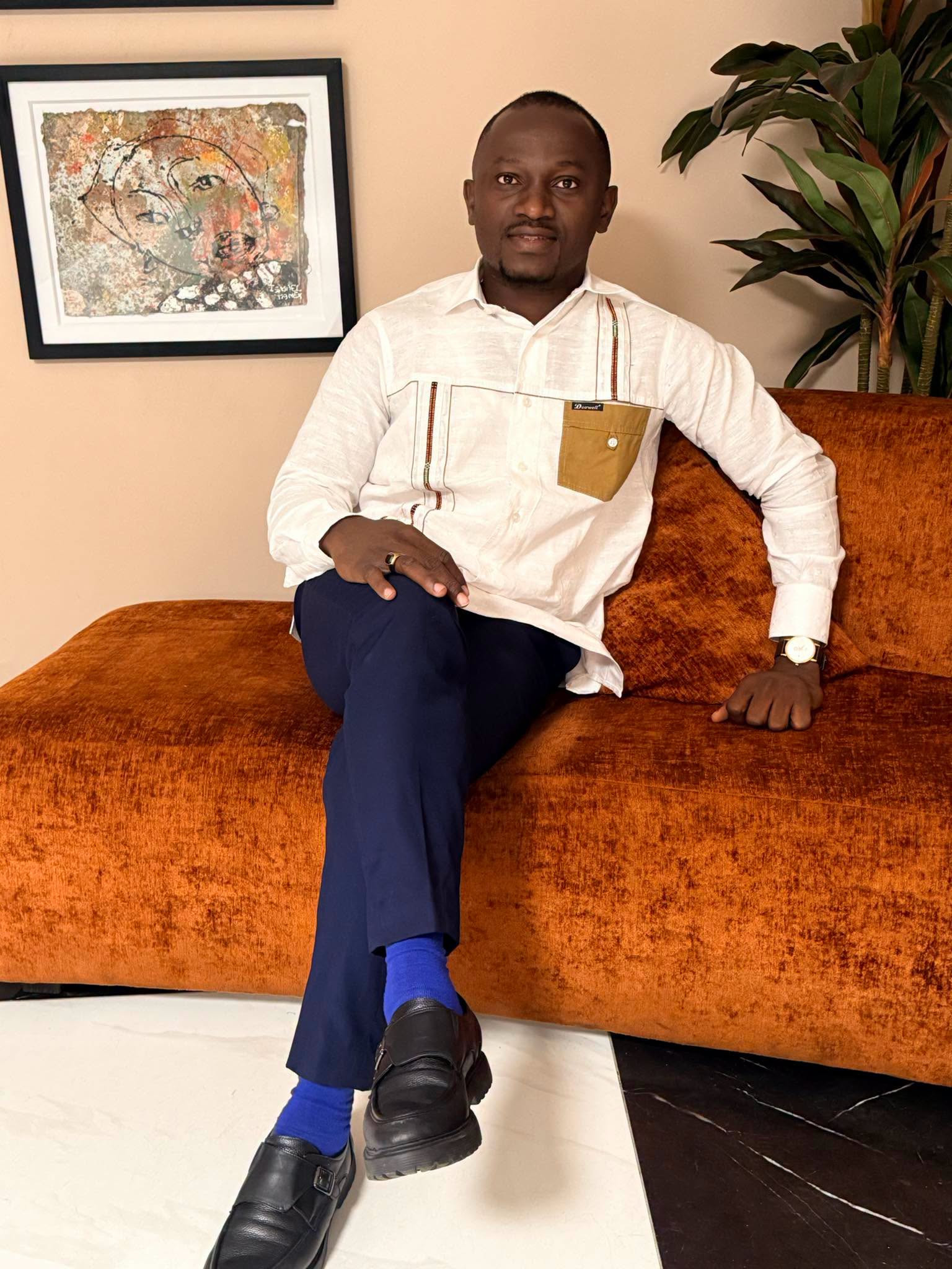 Portrait fourni de Date Kouakou Patrice, assis sur un canapé orange, en chemise blanche.