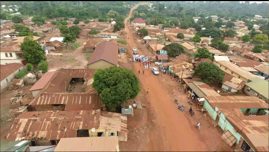Vue aérienne fournie montrant des habitations, une route en terre et un rassemblement.